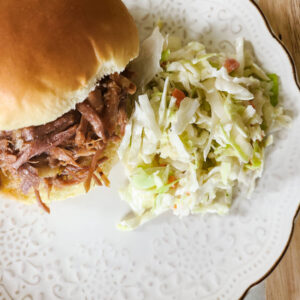 pulled pork sandwich with pile of coleslaw next to it on white plate with dark wood as backround.