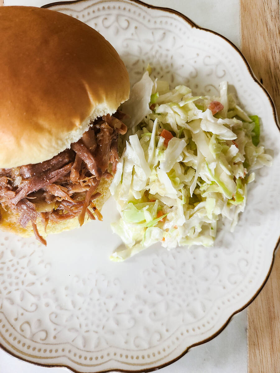 pulled pork sandwich with pile of coleslaw next to it on white plate with dark wood as backround.