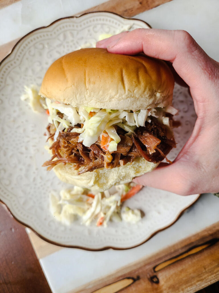 hand holding pulled pork bun with coleslaw on it. 