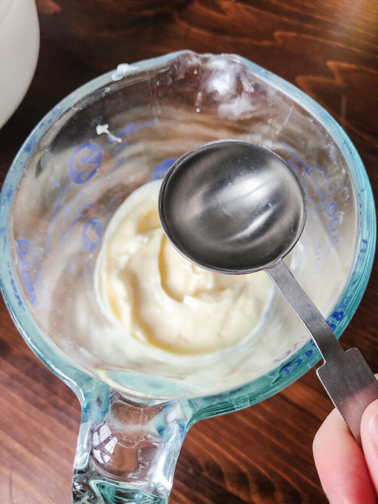 woman pouring vinegar into mayo using metal tablespoons 