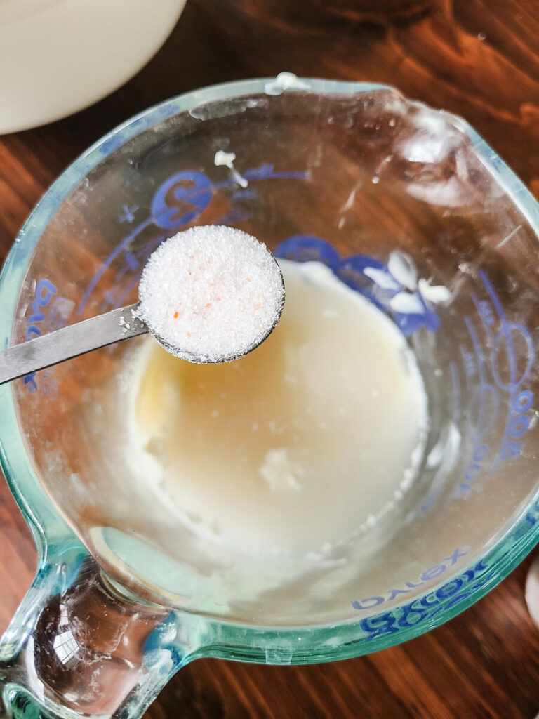 woman adding salt into liquid measuring cup with mayo and vinegar to make creamy coleslaw dressing 