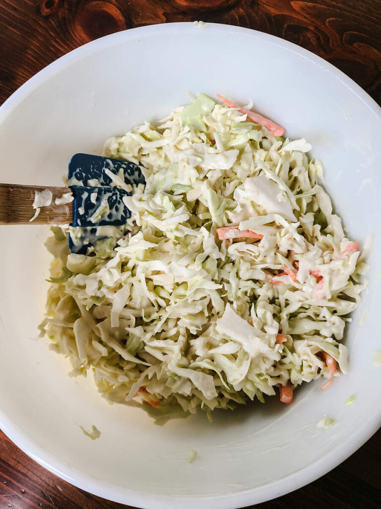 woman mixing big bowl of coleslaw with dark blue silicone spatula 