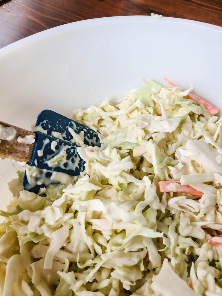 woman mixing the best coleslaw recipe with blue spatula in a white bowl 