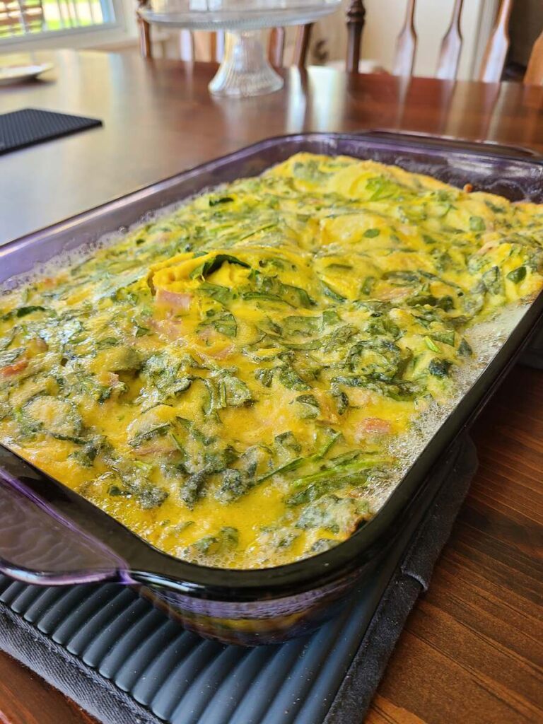 cooked pan of savory German pancake with ham and spinach resting on wood table with gray hot pads underneath 