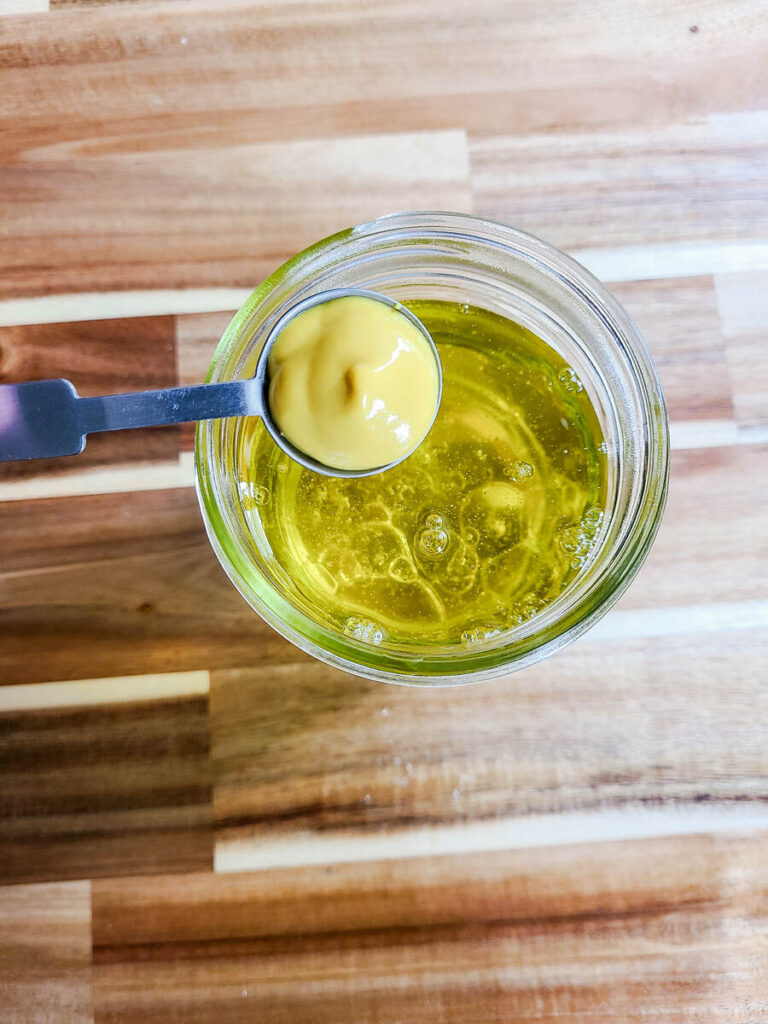 woman pouring measured mustard into oil mixture in jar 