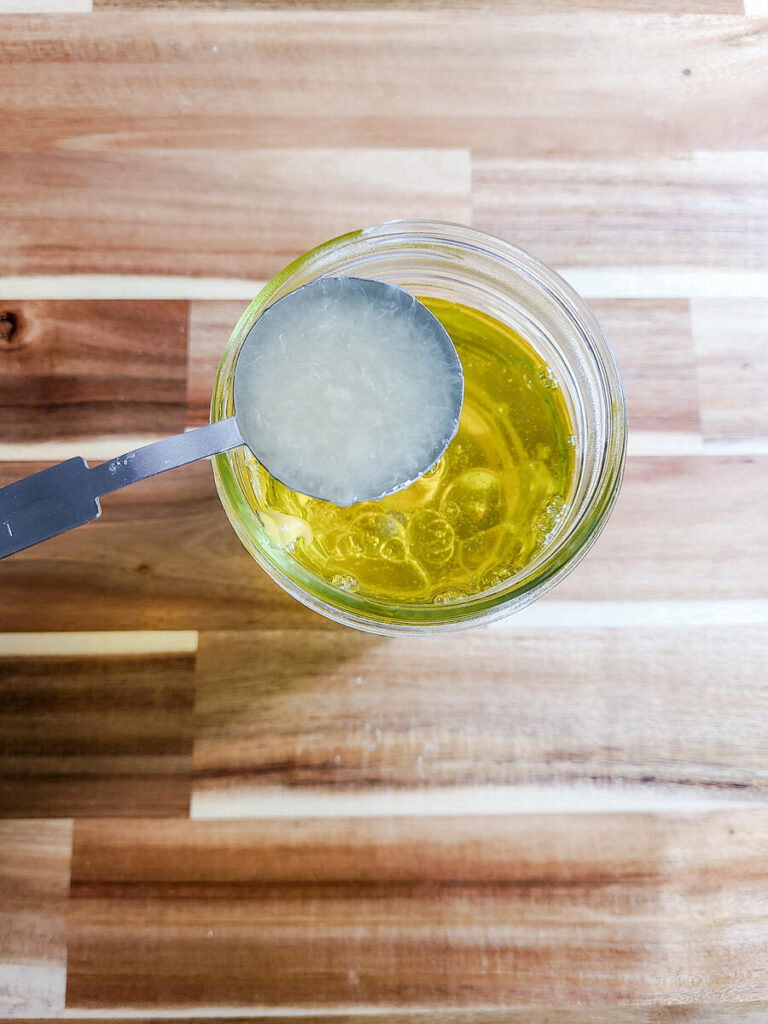 woman adding lemon juice to oil mixture in jar 