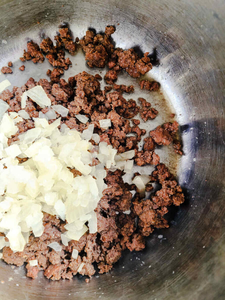 woman adding chopped onion to instant pot with cooked ground beef 