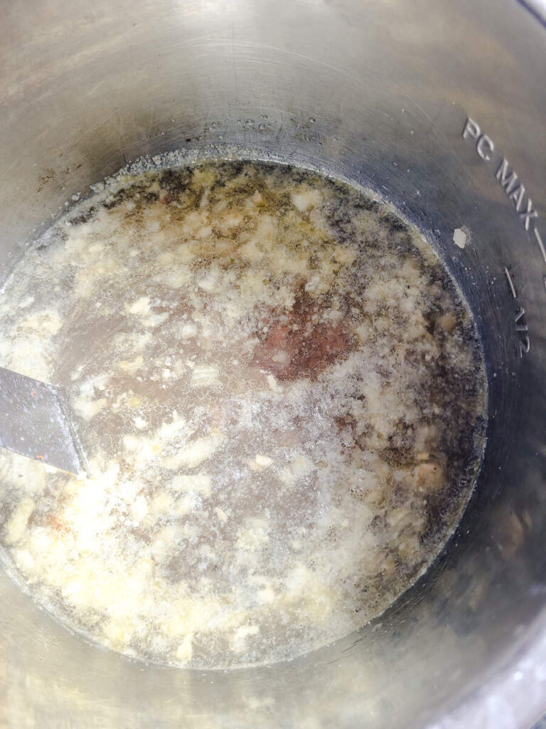 woman adding chicken broth to instant pot with cooked chopped onion and ground beef 