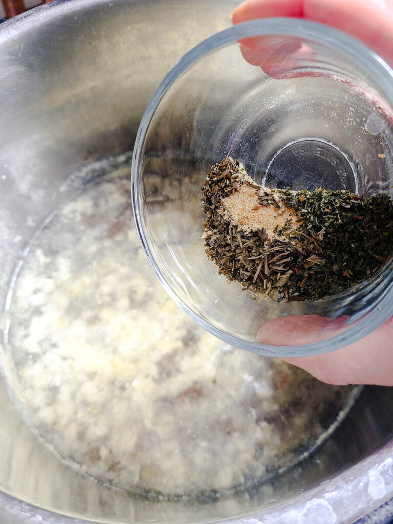 woman adding herbs, garlic powder, and salt to instant pot with broth, ground beef, and onions 