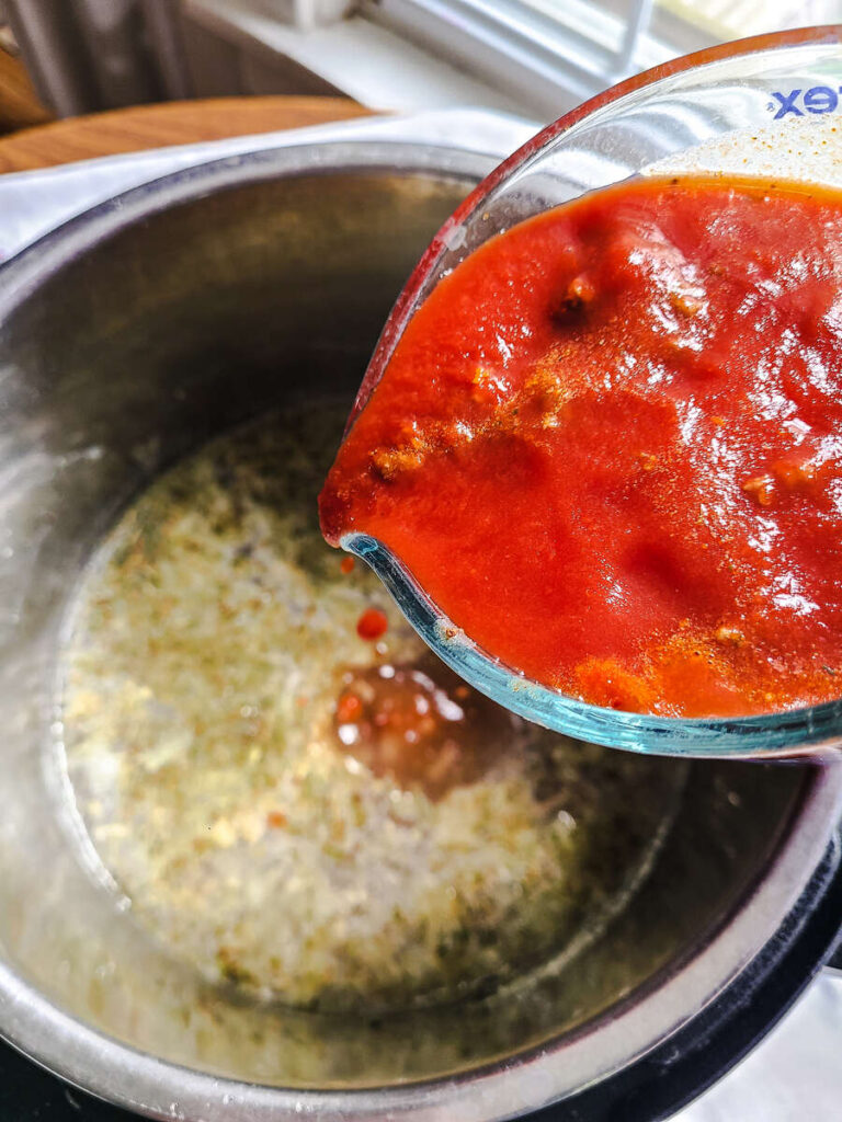 woman adding tomato sauce to pot with herbs, garlic powder, and salt to instant pot with broth, ground beef, and onions 