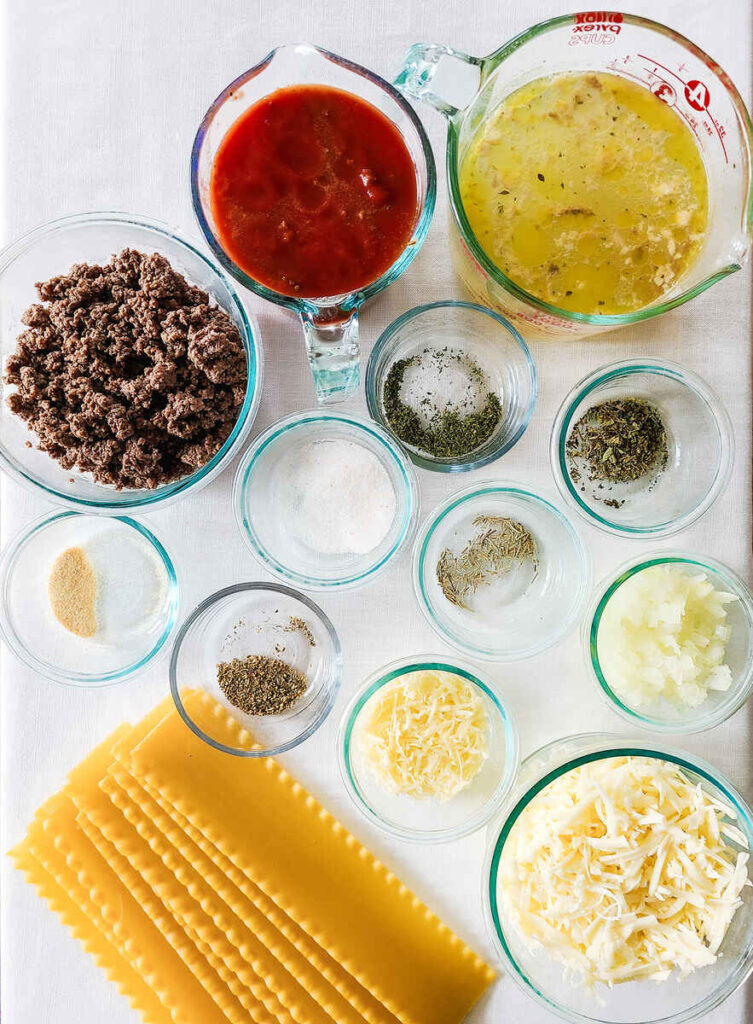 lasagna soup ingredients all laid out in glass containers on a white table cloth. 