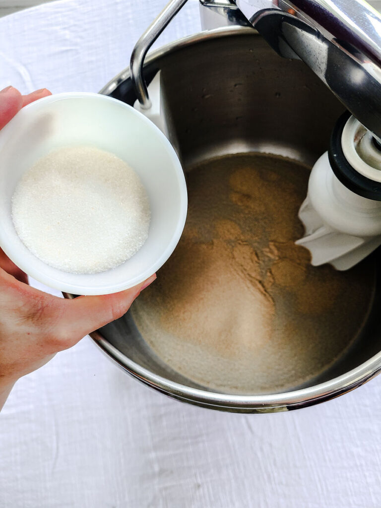 woman adding sugar to yeast and water mixture in standing mixer bowl 