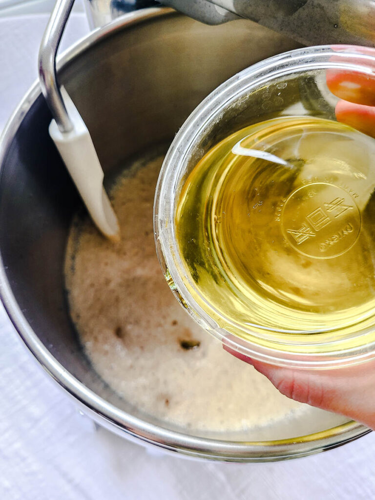 woman adding oil to yeast mixture in standing mixer bowl 