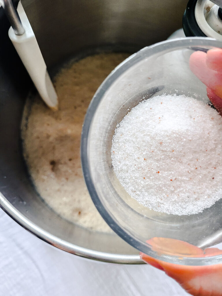 woman adding salt to yeast mixture in standing mixer bowl  