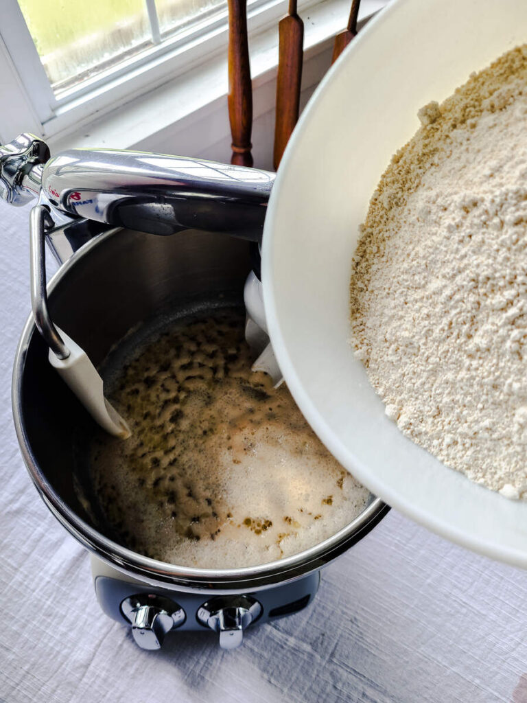 woman adding flour to yeast mixture in standing mixer bowl  
