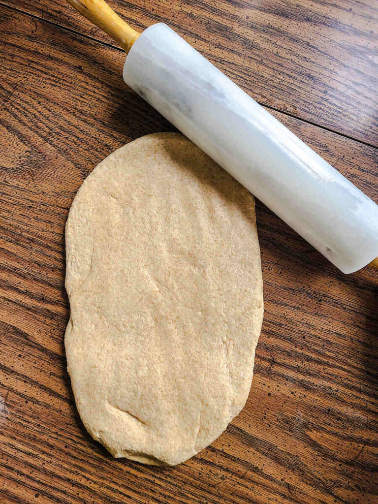 woman rolling bread dough into rectangle with marble rolling pin on wood table 