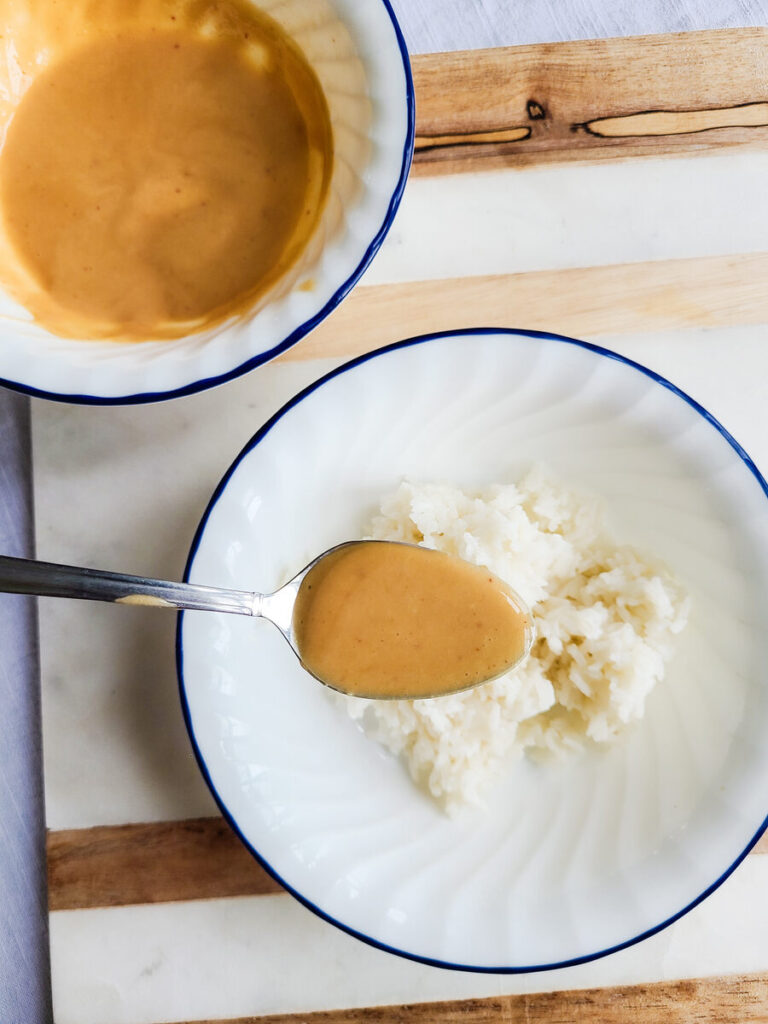 background of a marble and wood counter top with 2 white bowls with dark blue edge sitting next to each other one full of spicy kimchi mayo with a spoon and one full of cooked white rice.